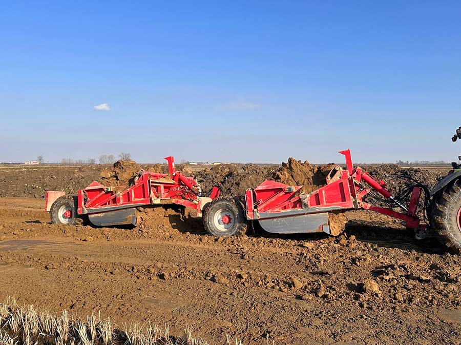 Tandem scraper agricolo trainato da trattore durante lavori di livellamento terreno